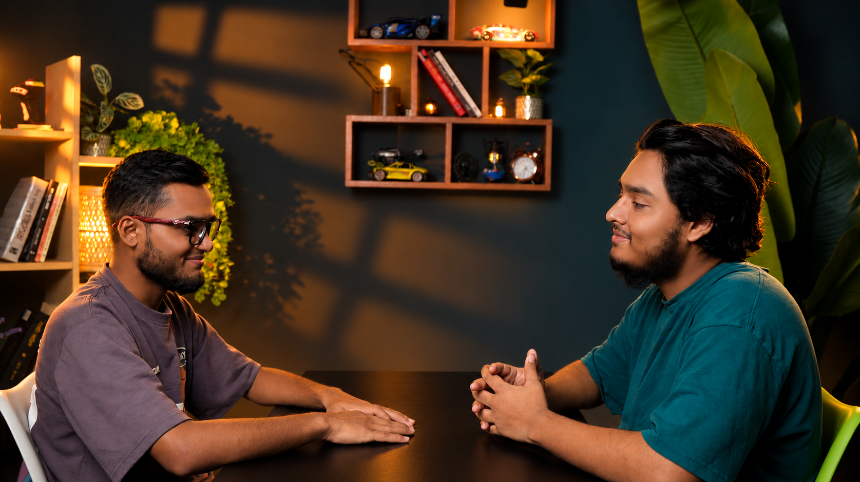 Two people in conversation at a table in the PlatiRoll studio with warm lighting, shelves and plants